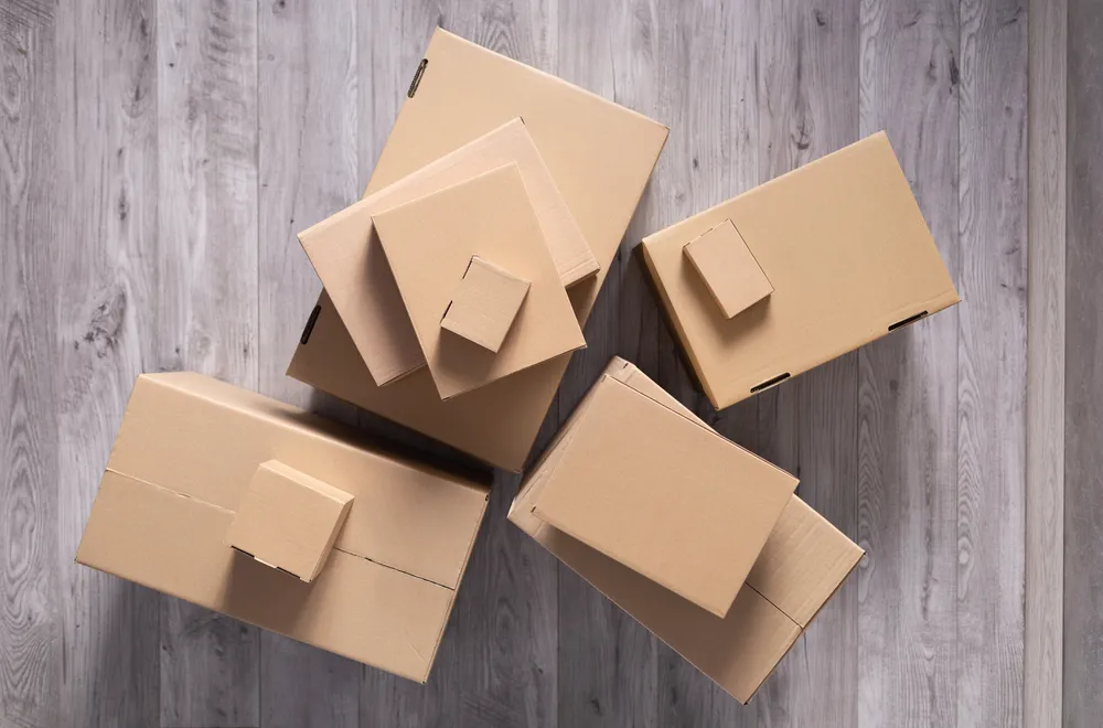 Vista superior de varias cajas de cartón Querétaro de distintos tamaños, apiladas sobre un piso de madera con tonos grises. 